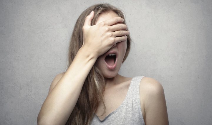 woman in gray tank top covering her face with her hand